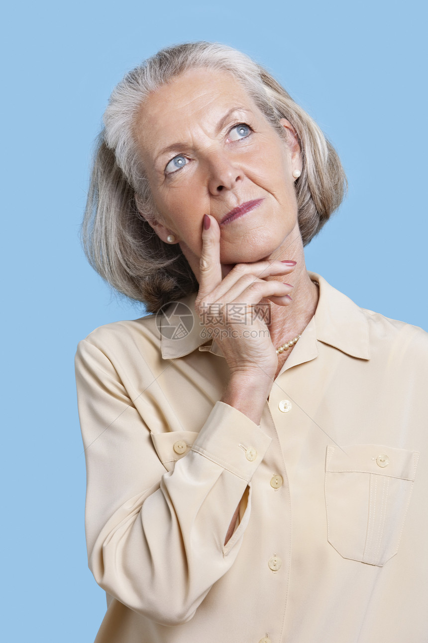 在蓝色背景下巴上手摸下巴的零工中 受争议高龄妇女影棚闲暇女性服装白发彩色短发休闲成人退休图片