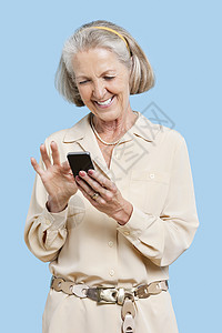 洼之三在蓝背景下在手机上读短信的微笑高龄妇女; 以蓝色背景阅读背景