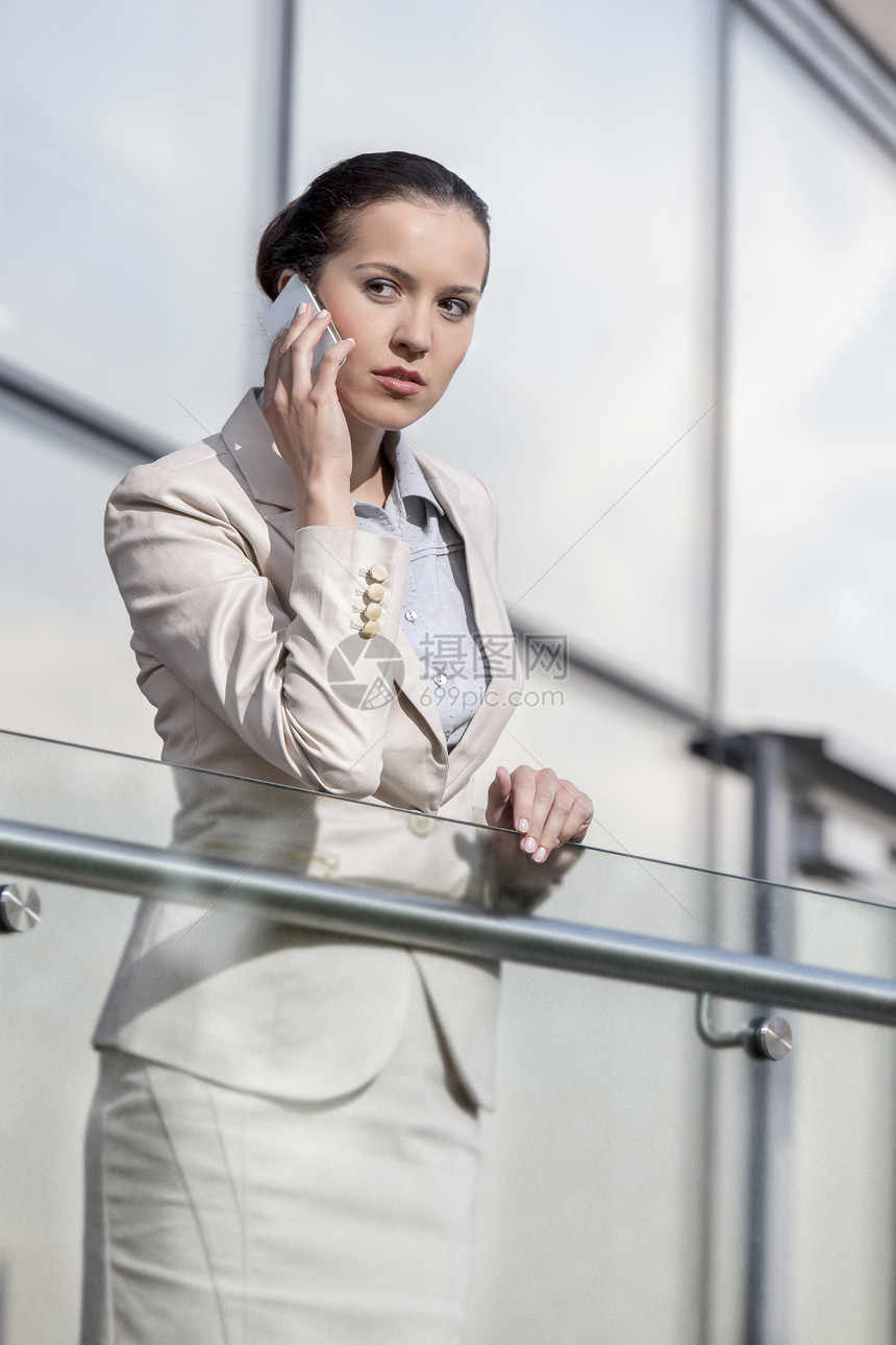 美丽的年轻女商务人士在办公室栏杆上使用智能电话图片