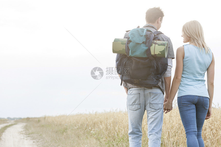 目睹年轻远足夫妇在农村步行时手牵手的景象背包风光田园远足者男性天空团结服装男朋友冒险图片