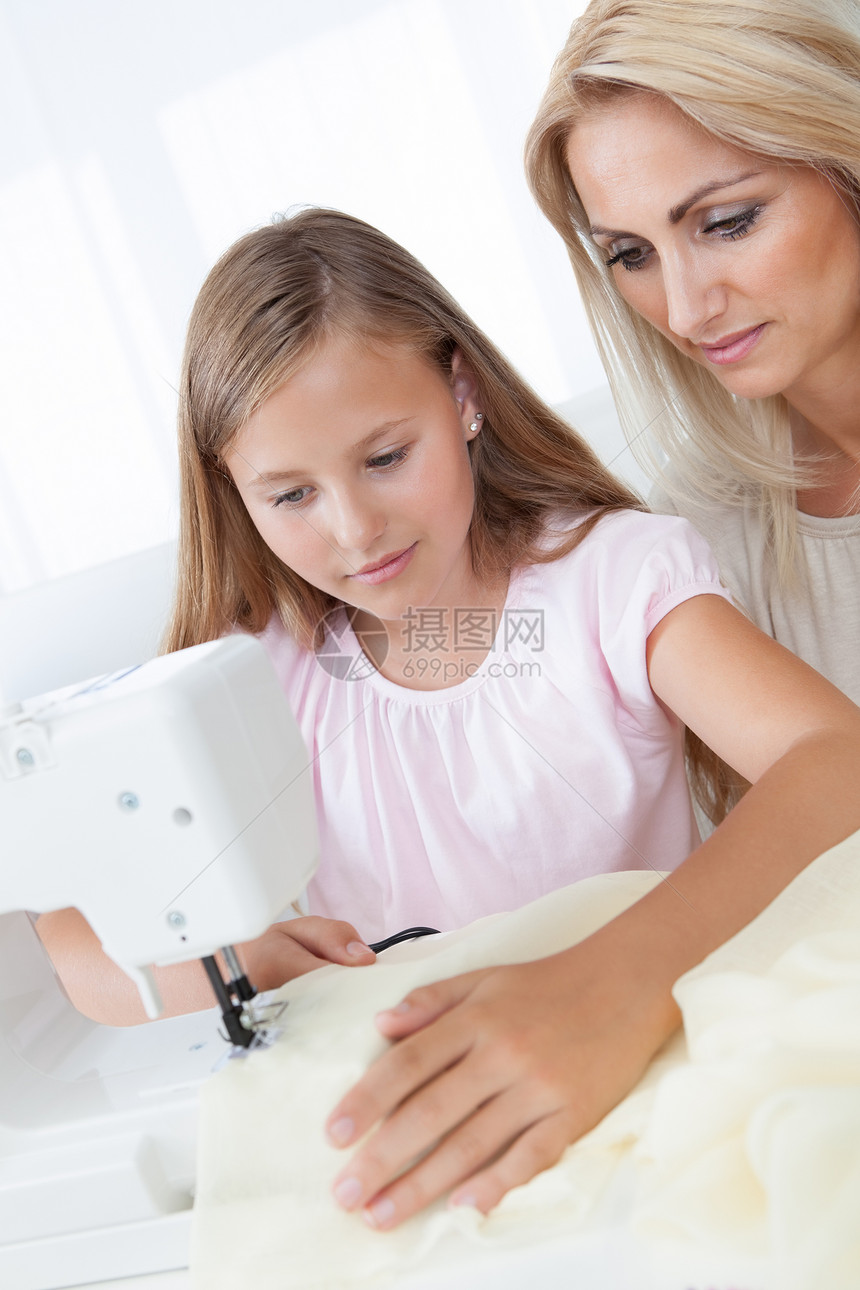 美丽的年轻女孩与母亲一起缝衣缝纫职业女士线程中年人学习工作别针机器衣服图片