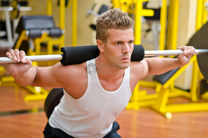 英俊的年轻人在健身房蹲下男人训练健美肌肉重量白色成人下蹲俱乐部建筑图片