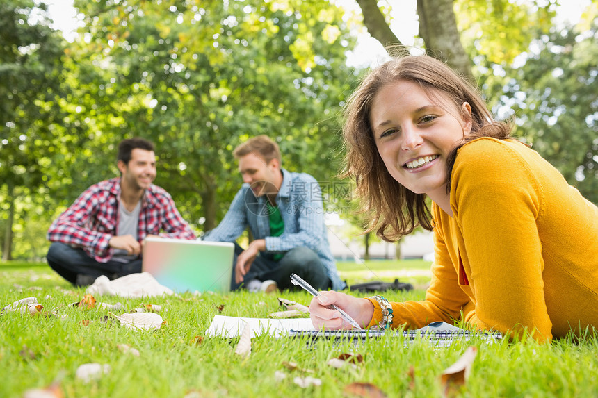 女性写笔记 学生在公园使用笔记本电脑朋友们大学友谊树木男性草地校园学习技术说谎图片