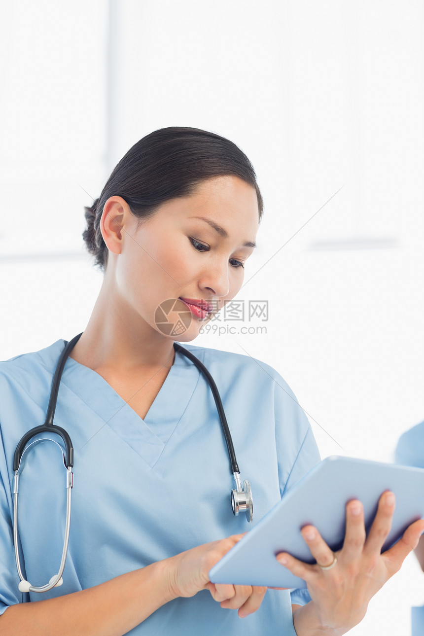使用数字片片子的美丽女性外科医生磨砂膏制服平板医疗药片触摸屏医院滚动电脑医务室图片