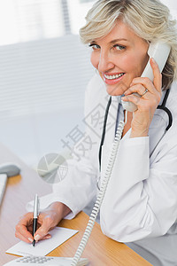 撰写笔记时使用电话的女医生诊所呼唤服务医务室保健职场固定电话短发写作卫生背景图片