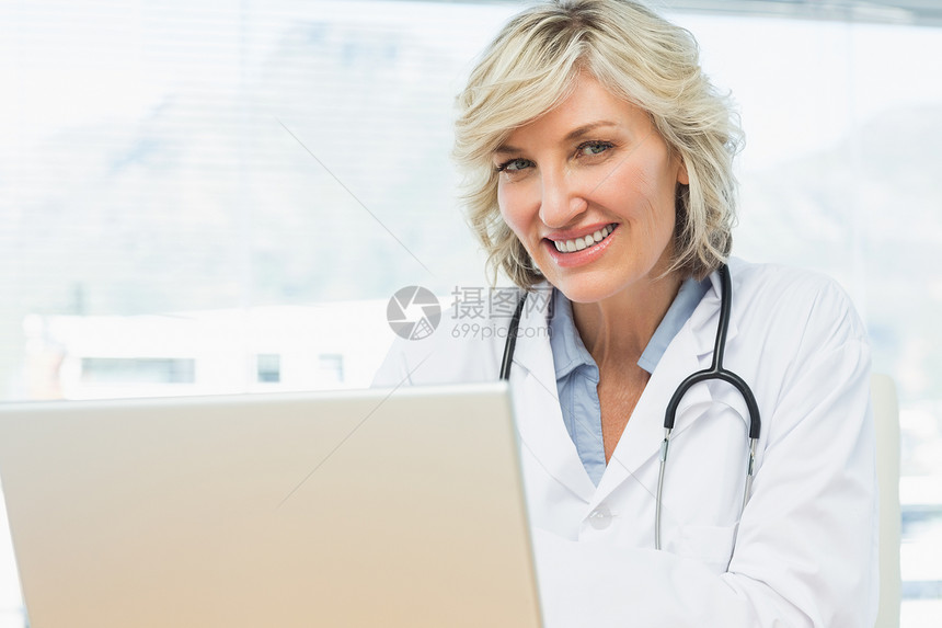 在医疗办公室使用膝上型电脑对女医生微笑图片