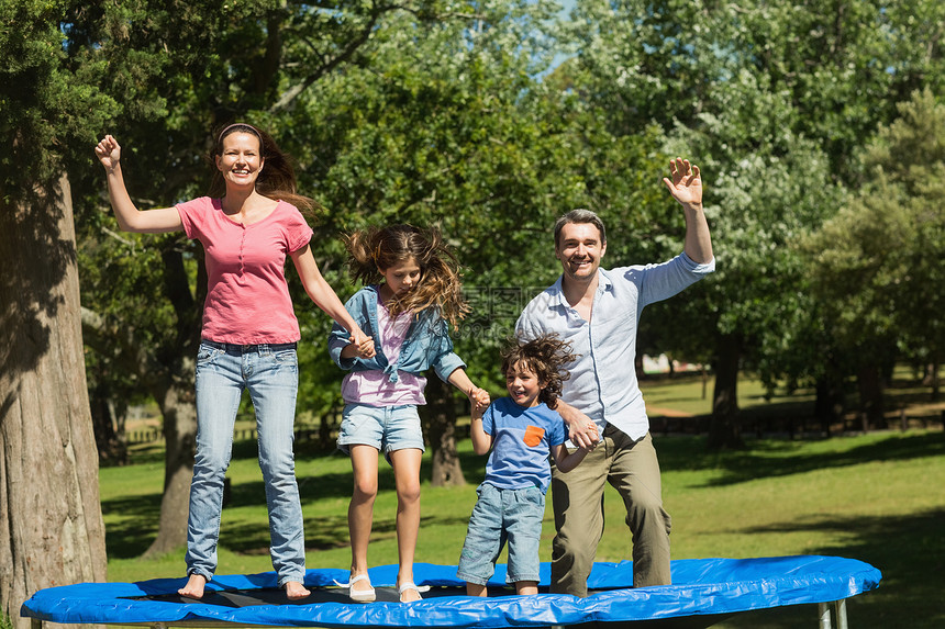 幸福的家庭在公园的蹦床上跳高图片