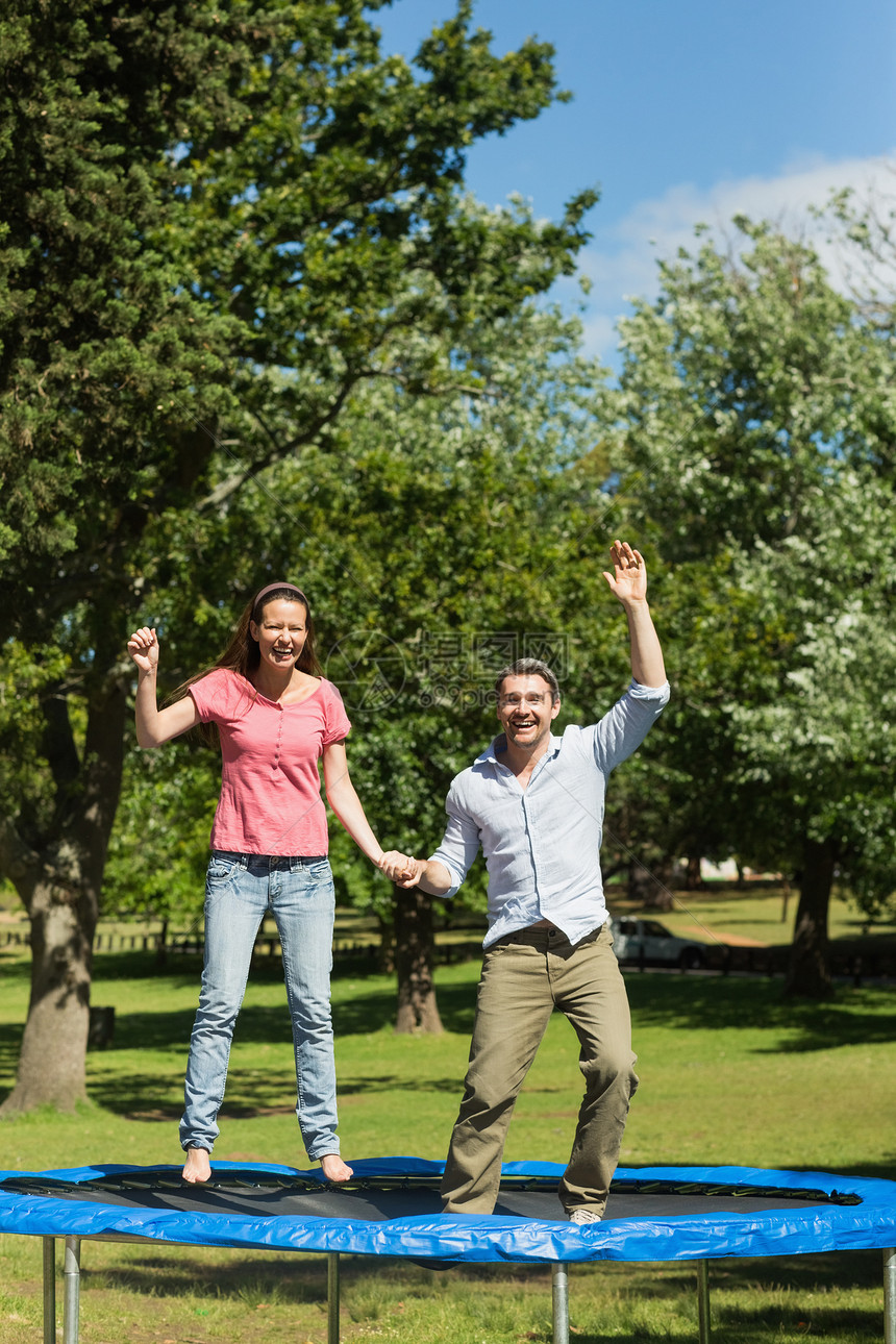 快乐的一对情侣跳高 在公园的蹦床上跳图片