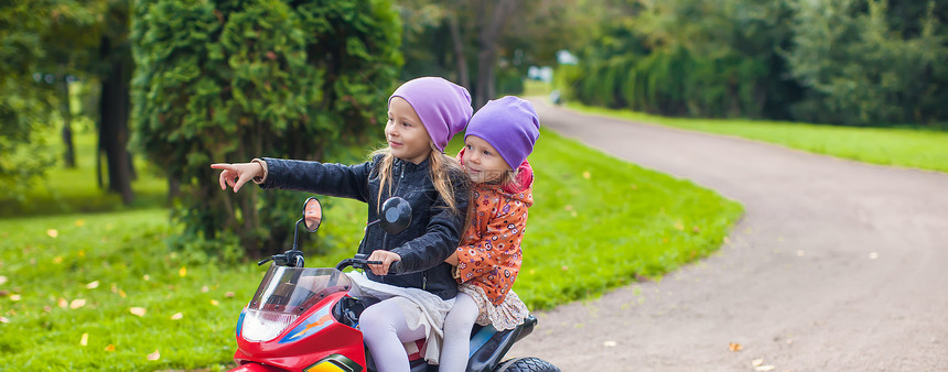 可爱的小女孩骑着孩子的自行车 在绿公园里游戏活动童年运动姐姐晴天微笑速度摩托车喜悦图片