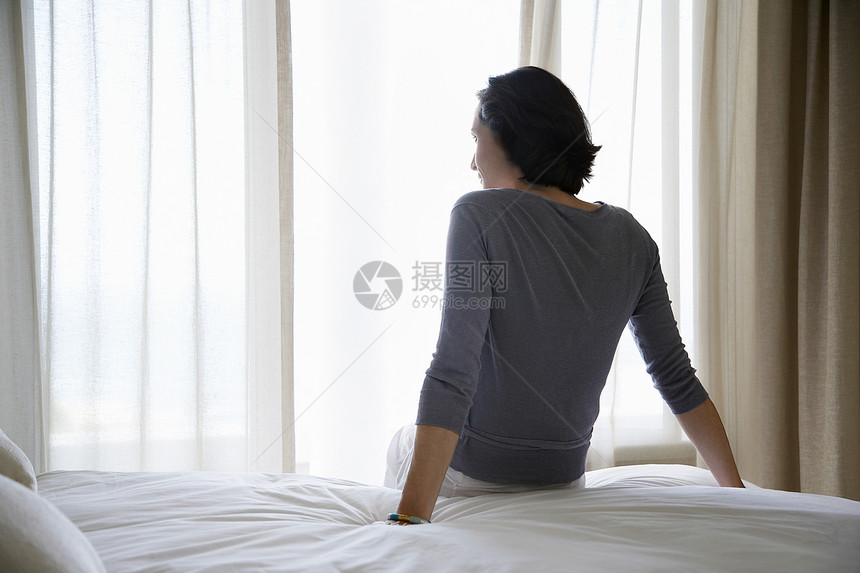 坐在床后视线上看窗边的女人图片