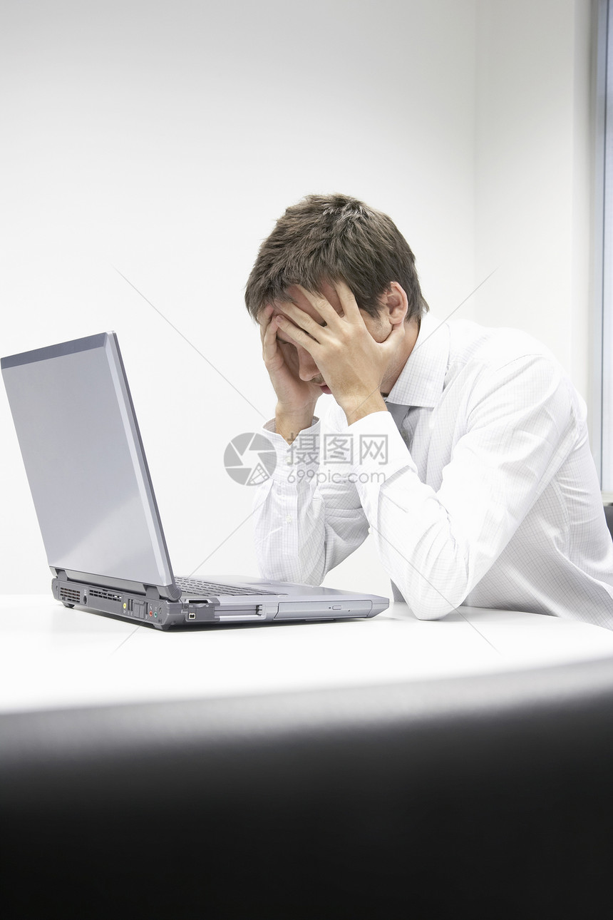 用膝上型电脑坐在书桌的有压力的商务人士图片