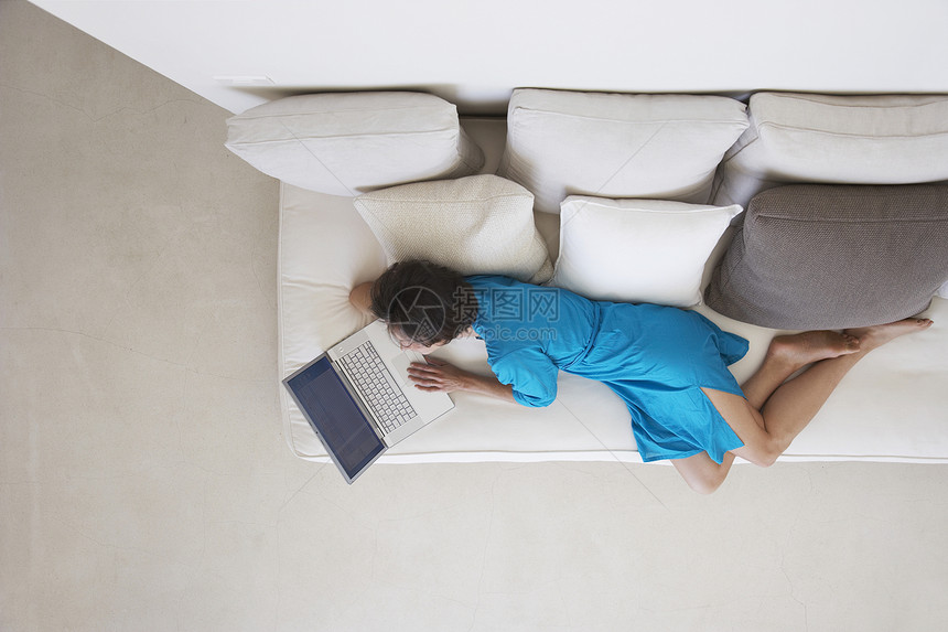 在客厅沙发上使用笔记本电脑的妇女被直接拍到技术地面互联网地板水平房子闲暇白色长椅软垫图片