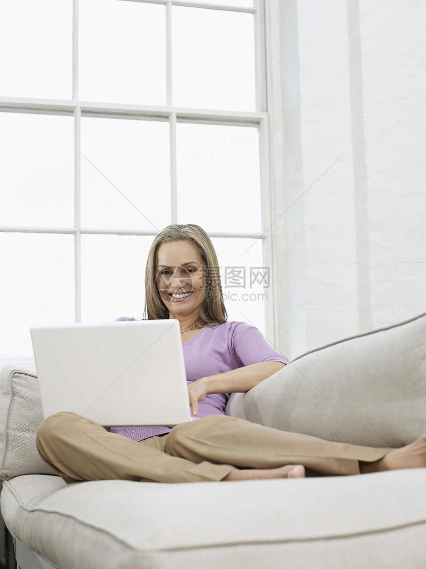 在沙发上使用笔记本电脑的中成年妇女图片
