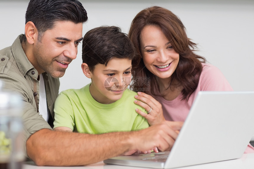 使用笔记本电脑与儿子一起微笑的一对夫妇学习技术孩子家庭父亲童年男人父母母亲厨房图片