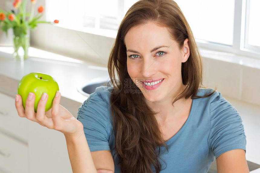 在厨房里拿着苹果的微笑的年轻女子图片