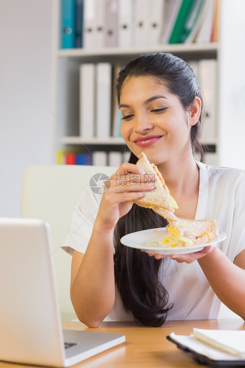 女商务人士在看笔记本电脑时有三明治图片