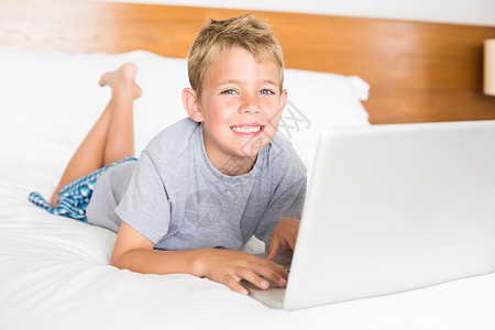 用笔记本电脑躺在床上的金发快乐男孩背景图片