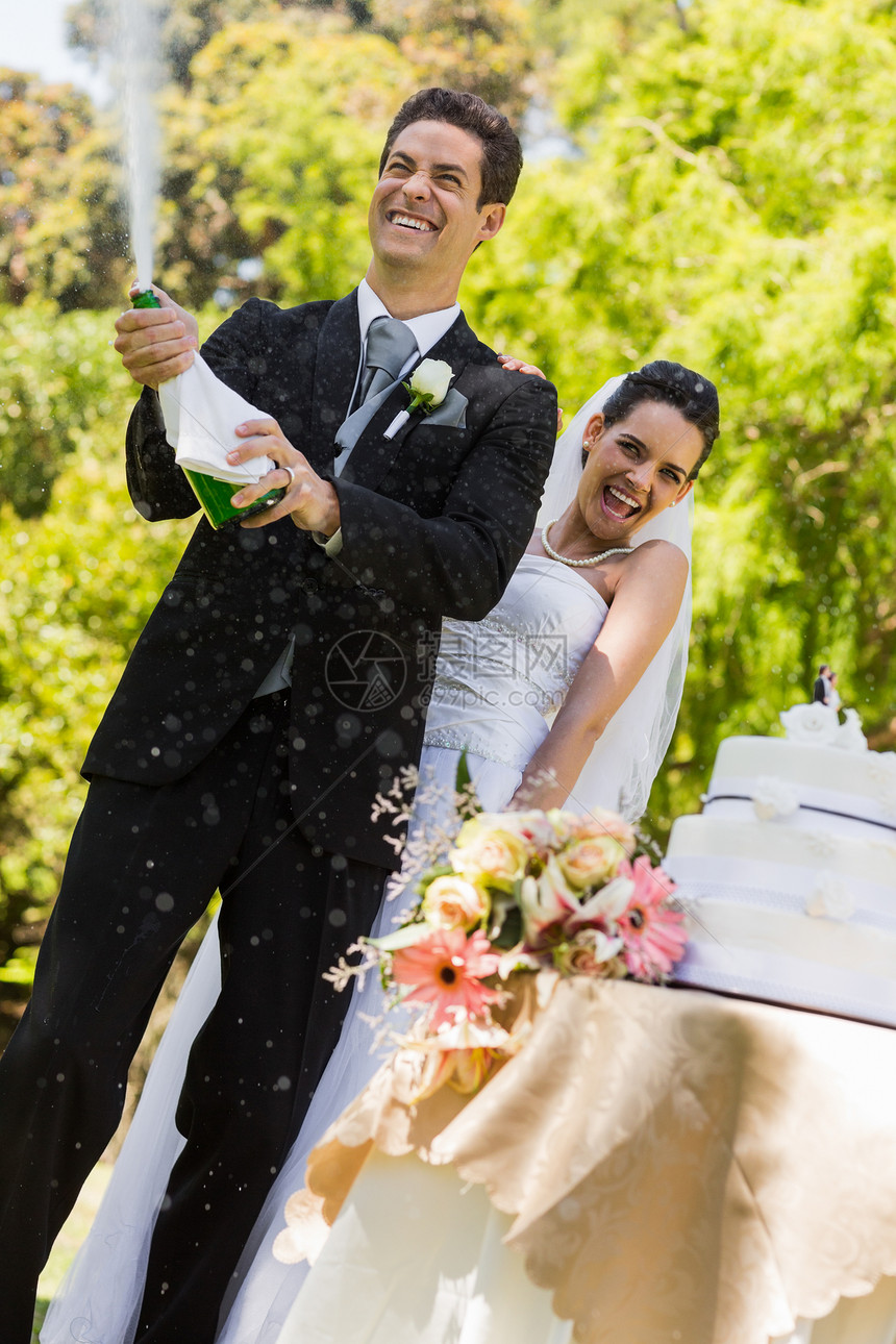 新婚夫妇和新郎在公园开香槟酒瓶婚礼裙子夫妻蛋糕婚纱男人树木团结丈夫奢华图片