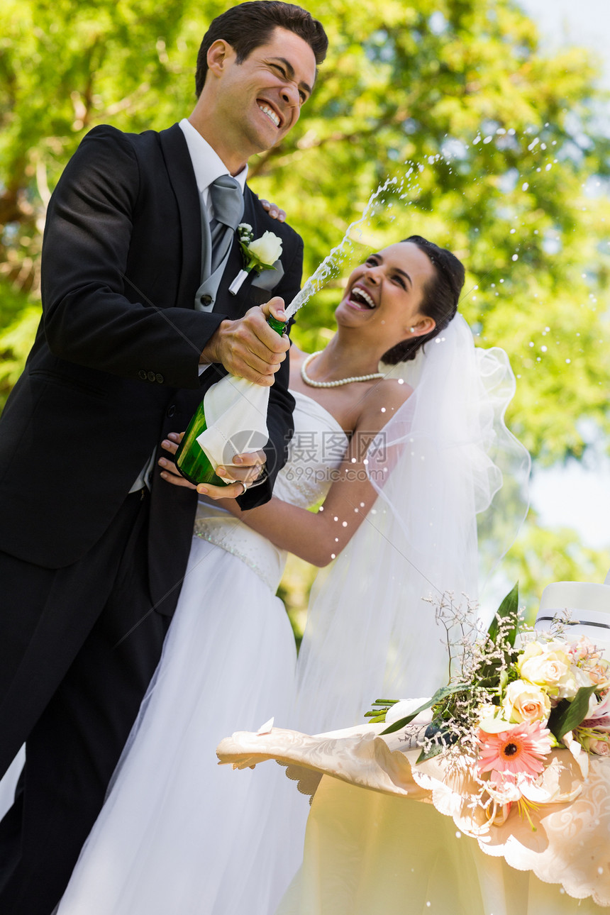 新婚夫妇和新郎在公园开香槟酒瓶喜悦团结男人婚礼丈夫酒精庆典联盟快乐花束图片