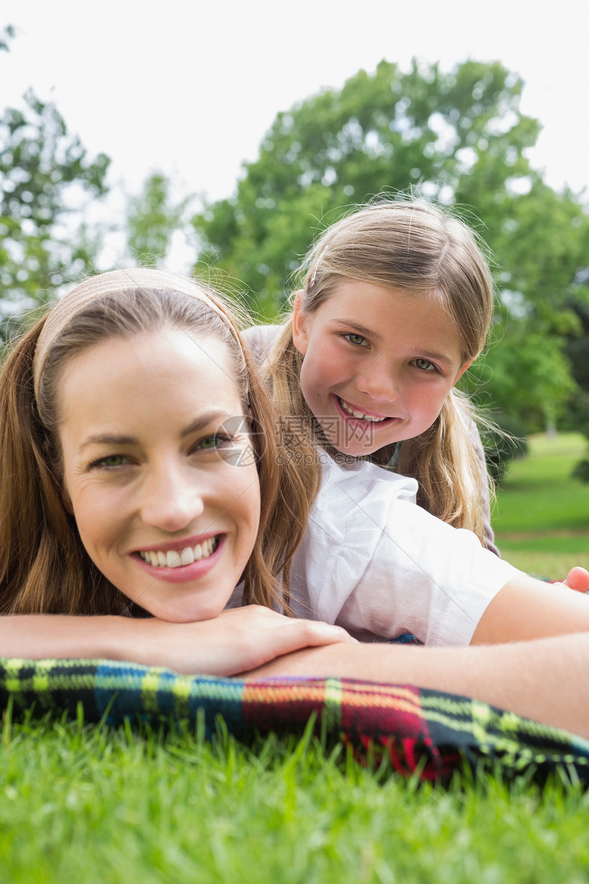 快乐的母亲和女儿躺在公园里的女儿微笑童年女性女士花园草地说谎女孩毯子树木图片