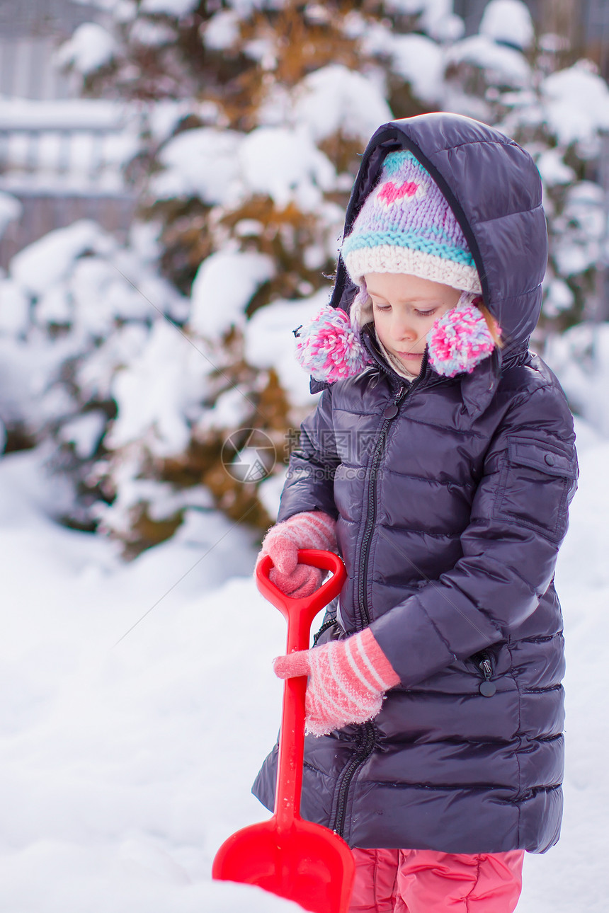 小女孩在花园里玩红铲子的小姑娘微笑快乐森林童年雪堆公园手套幸福闲暇季节图片