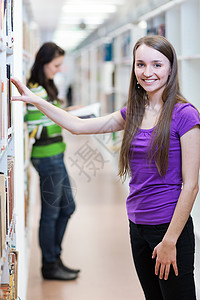 在图书馆  漂亮 女学生在寻找书本青年笔记本学生美丽教育班级微笑技术家庭作业电脑背景图片