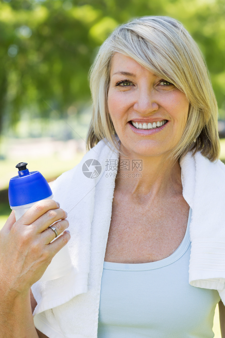 妇女在公园中拥有水瓶绿地浅色时间成人毛巾运动服瓶子闲暇女性金发女郎图片