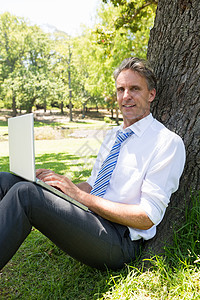 自信的商务人士 在公园用笔记本电脑闲暇男性休息树干生意人人士技术衬衫沟通商务背景图片