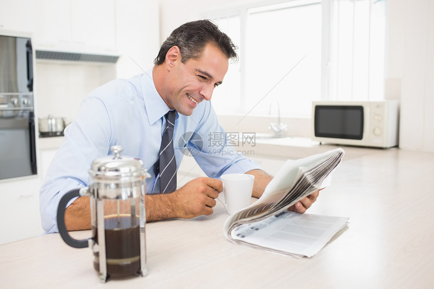 在厨房用喝咖啡杯的阅读报纸微笑着身穿盛装的男人图片