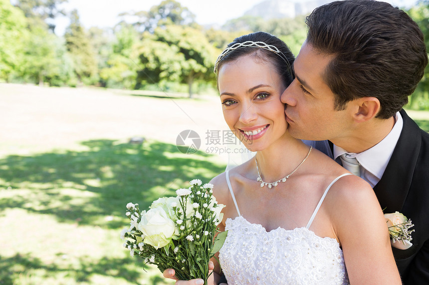 Groom 亲吻花园中脸颊上美丽的新娘图片