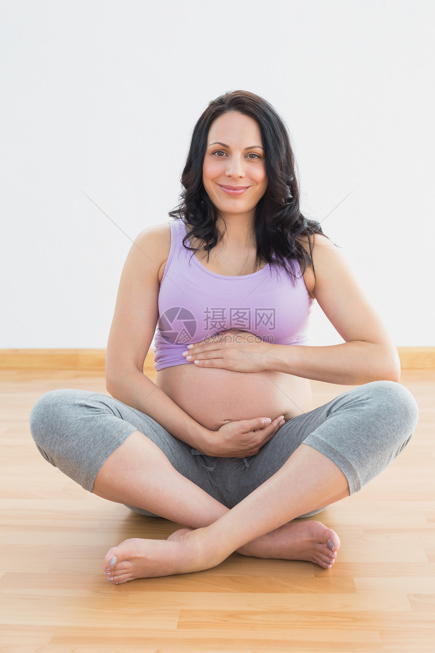 坐在地板上 抱着肚子的孕妇对着镜头微笑图片
