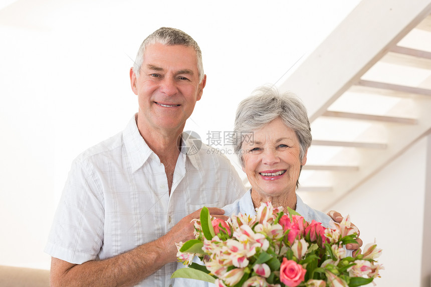 高龄夫妇对着拿着花束的照相机微笑图片