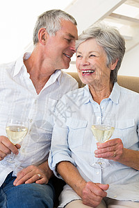 坐在沙发上喝白酒的年长夫妇闲暇房子成人家庭流金退休男性客厅男人微笑背景图片
