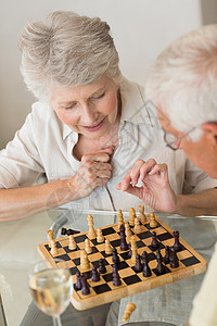 玩象棋和喝白酒的老夫妇微笑棋盘快乐酒精男性住所酒杯老年退休家庭厨房背景图片