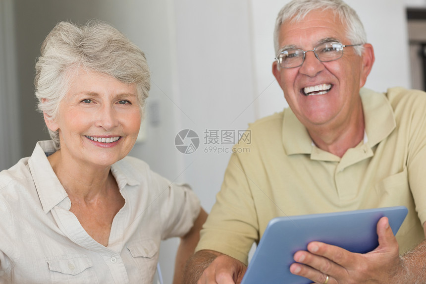 在餐桌上使用平板电脑的快乐老年情侣微笑住所桌子夫妻闲暇男性女性头发家庭公寓图片