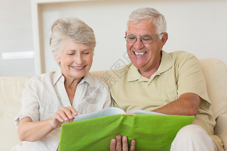 在沙发上一起看相册的 快乐的老年情侣相片集乡愁家庭回忆成人闲暇男性退休微笑夫妻背景图片