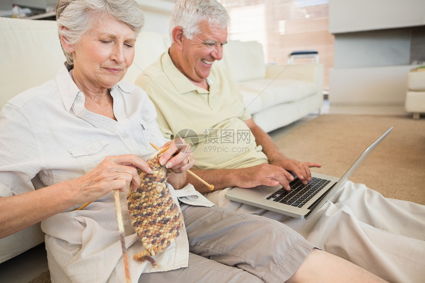 坐在地板编织和使用笔记本电脑的老夫妇女士公寓闲暇老年房子小地毯成人技术家庭男人图片