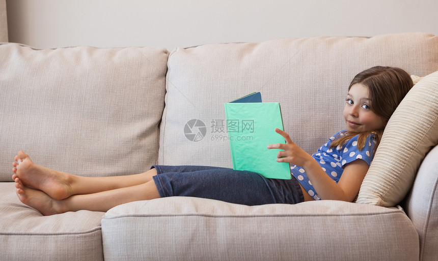 一位年轻女孩在沙发上读书的肖像图片