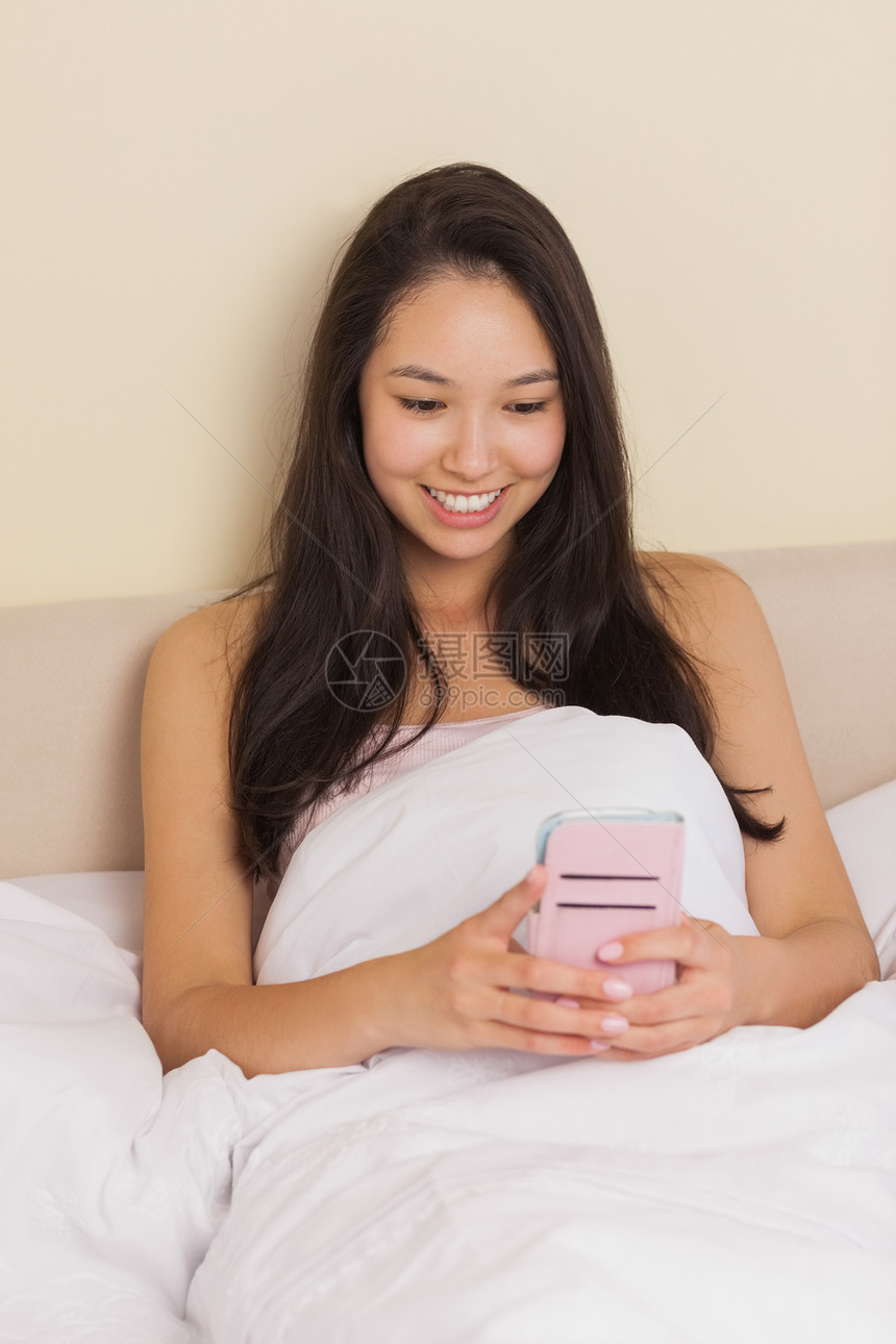 使用智能手机坐在床上的年轻亚洲妇女图片