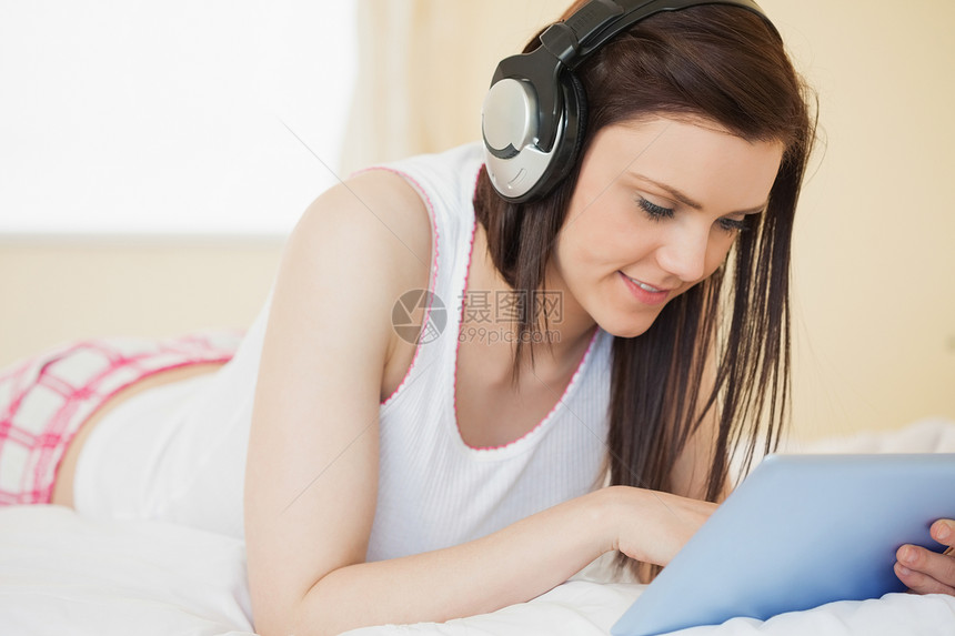微笑的女孩在听音乐 用躺在床上的平板电脑图片