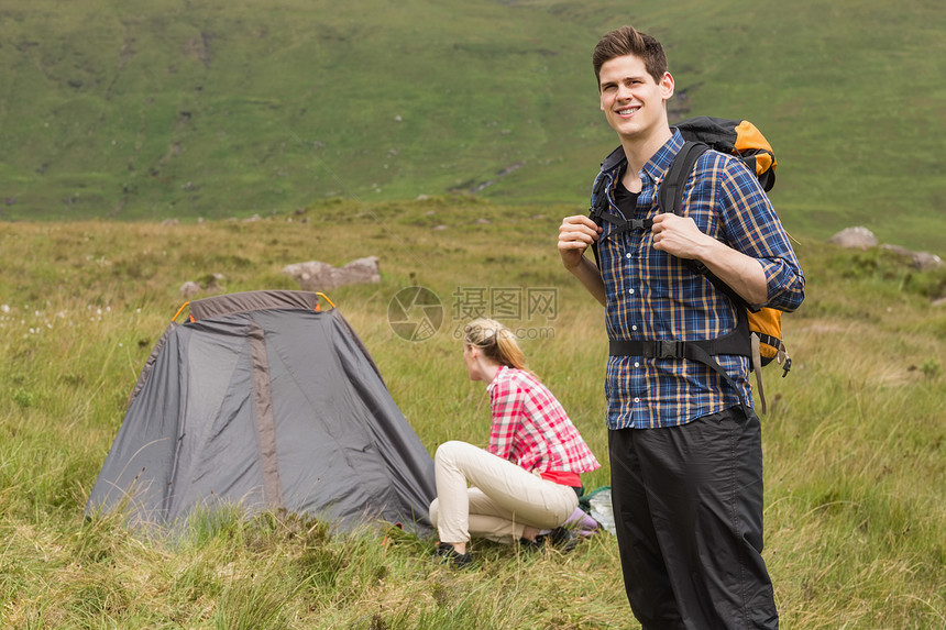 微笑的男人背着背包 而女朋友在搭帐篷图片