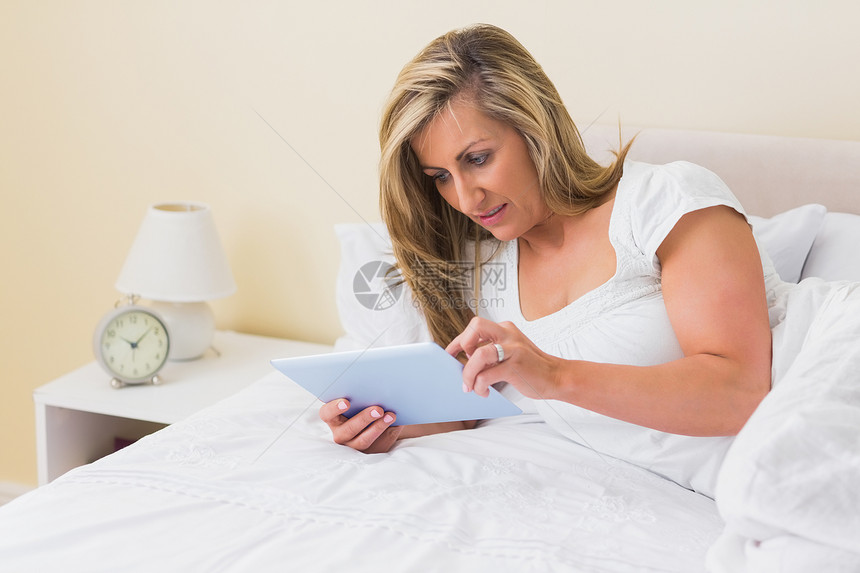 利用躺在床上的平板纸片的女人金发公寓快乐住所滚动女士闲暇女性长发房子图片
