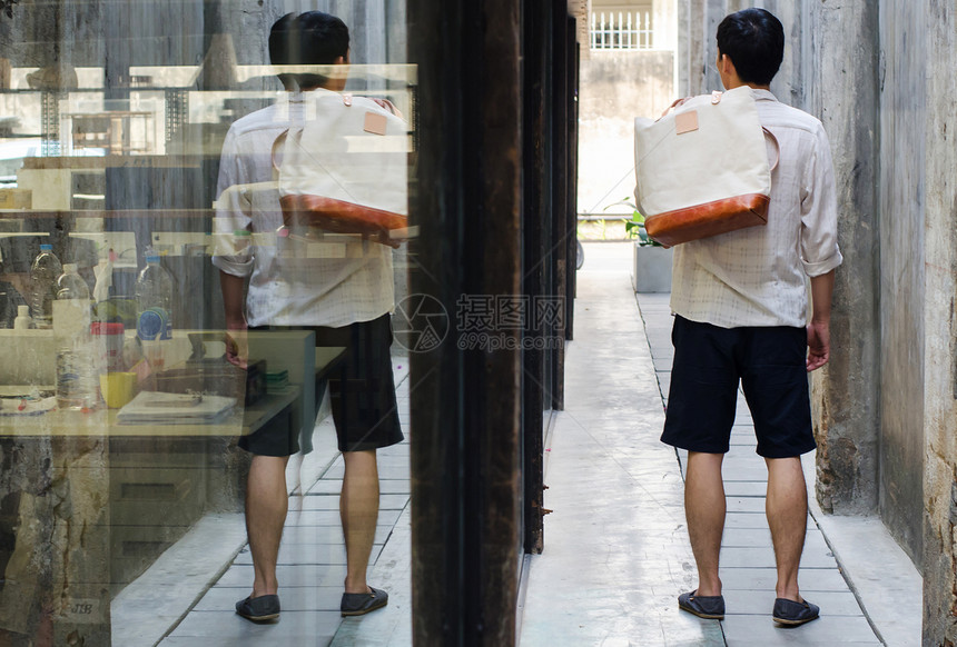 在水泥墙上挂着帆布袋的亚洲人图片