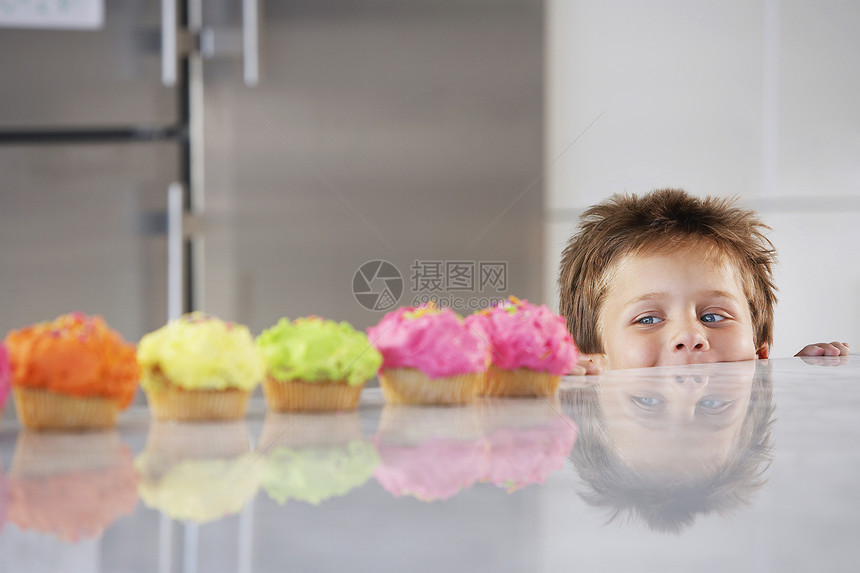 小男孩在厨房的一排纸杯蛋糕柜台偷看图片