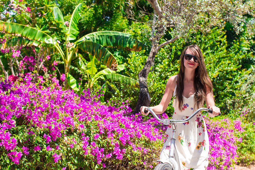在美丽的花园的热带度假胜地骑自行车的年轻女子图片