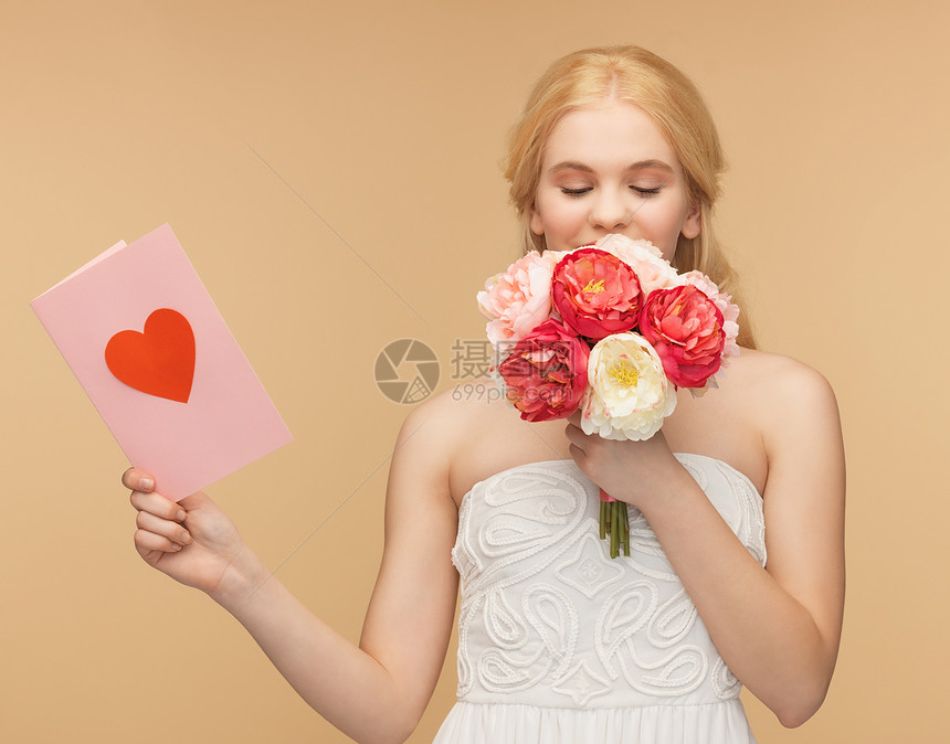 女孩闻着鲜花的香味和持有明信片图片