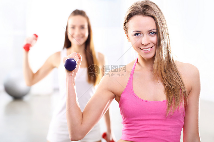在健身房培训有重体重的两名年轻妇女皮肤肌肉娱乐夹克活力微笑哑铃女孩朋友女士图片