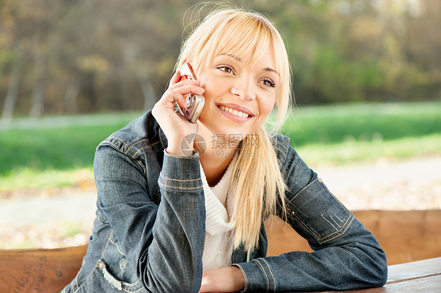 在公园里打个电话的女人牛仔裤微笑成人金发女性享受图片