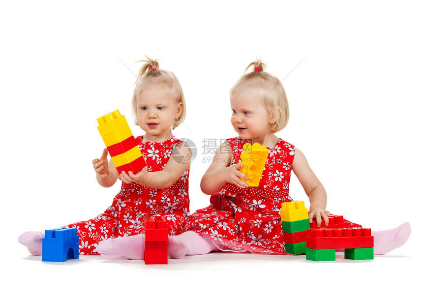 两个身穿红裙子的双胞胎女孩 玩砖块游戏幼儿园立方体家庭童年玩具姐妹闲暇女儿们女性孩子图片