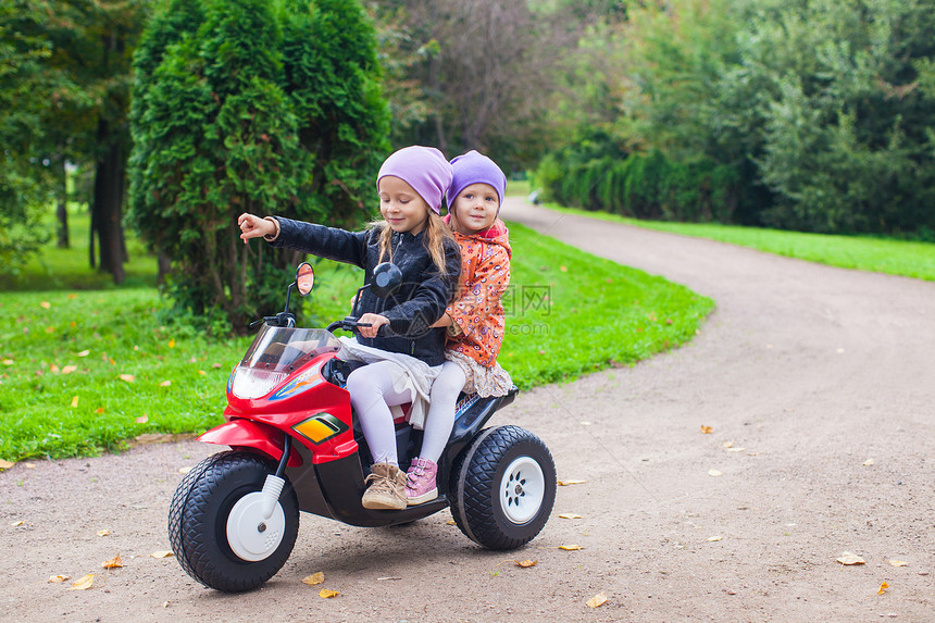 可爱的小女孩 在绿色公园骑着孩子的摩托车婴儿晴天玩具自行车姐姐游戏女孩童年运输裙子图片